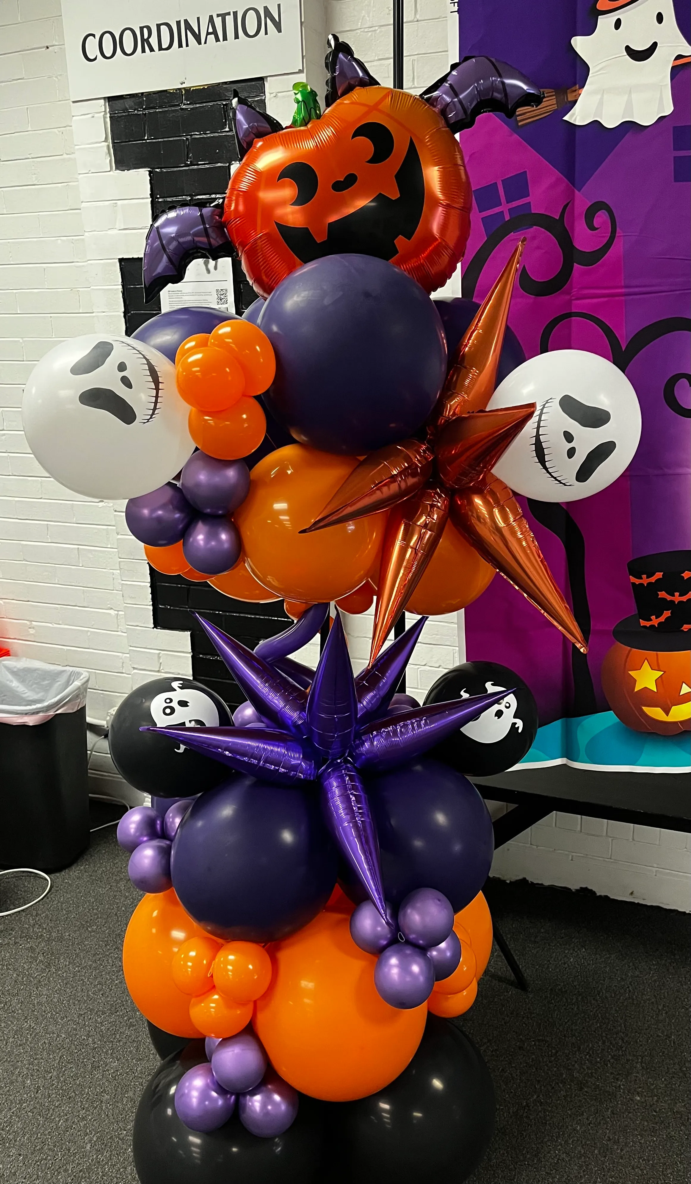 Halloween balloon pillar with pumpkin topper and purple, orange, and black balloon clusters.